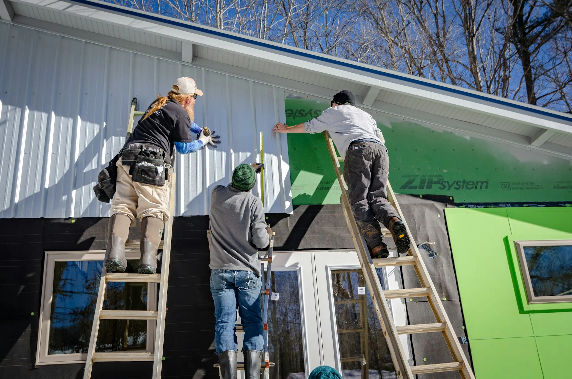 Workers on ladders fitting sheathing to the side of a house