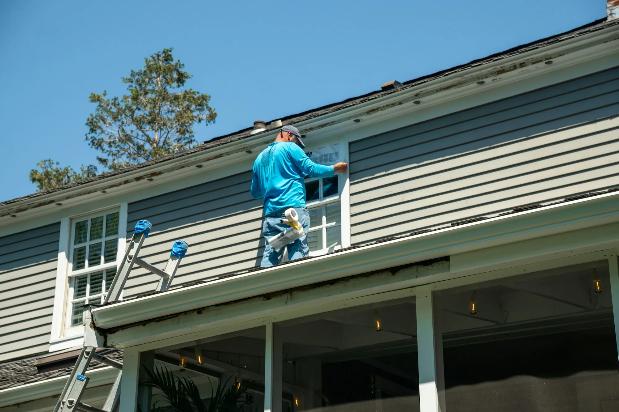 Contractor on a ladder working just below the roof edge